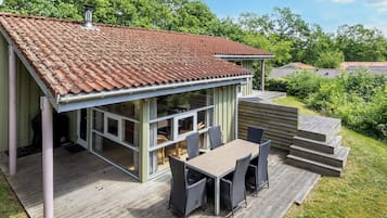 A house with a tiled roof, a deck with a table and chairs, and a view of the surrounding greenery.