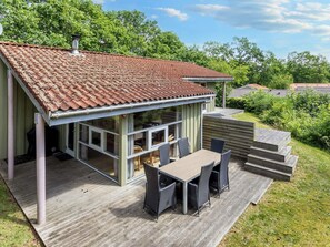 A house with a tiled roof, a deck with a table and chairs, and a view of the surrounding greenery.