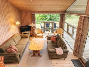 Un salon chaleureux avec un décor intérieur en bois, une télévision, deux canapés, une table basse et une vue sur l’extérieur.