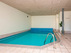 An indoor swimming pool with clear blue water, tiled floor, and metal handrails.
