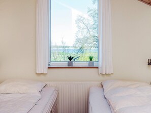 Een kamer met twee bedden, een raam met gordijnen en twee potplanten op de vensterbank.