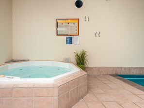 A hot tub in a room with tiled flooring, a potted plant, and informational posters on the wall.