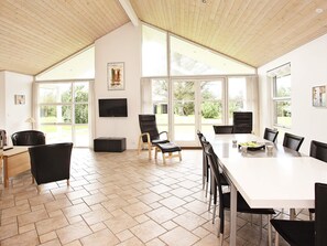 Un espacio amplio con una gran mesa de comedor, múltiples sillas, un televisor y ventanas grandes que ofrecen vistas al exterior.