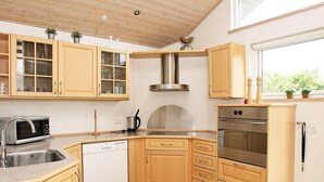 Eine kleine Küche mit Holzschränken, einer Edelstahl-Dunstabzugshaube, einem eingebauten Geschirrspüler und einem Fenster für natürliches Licht.