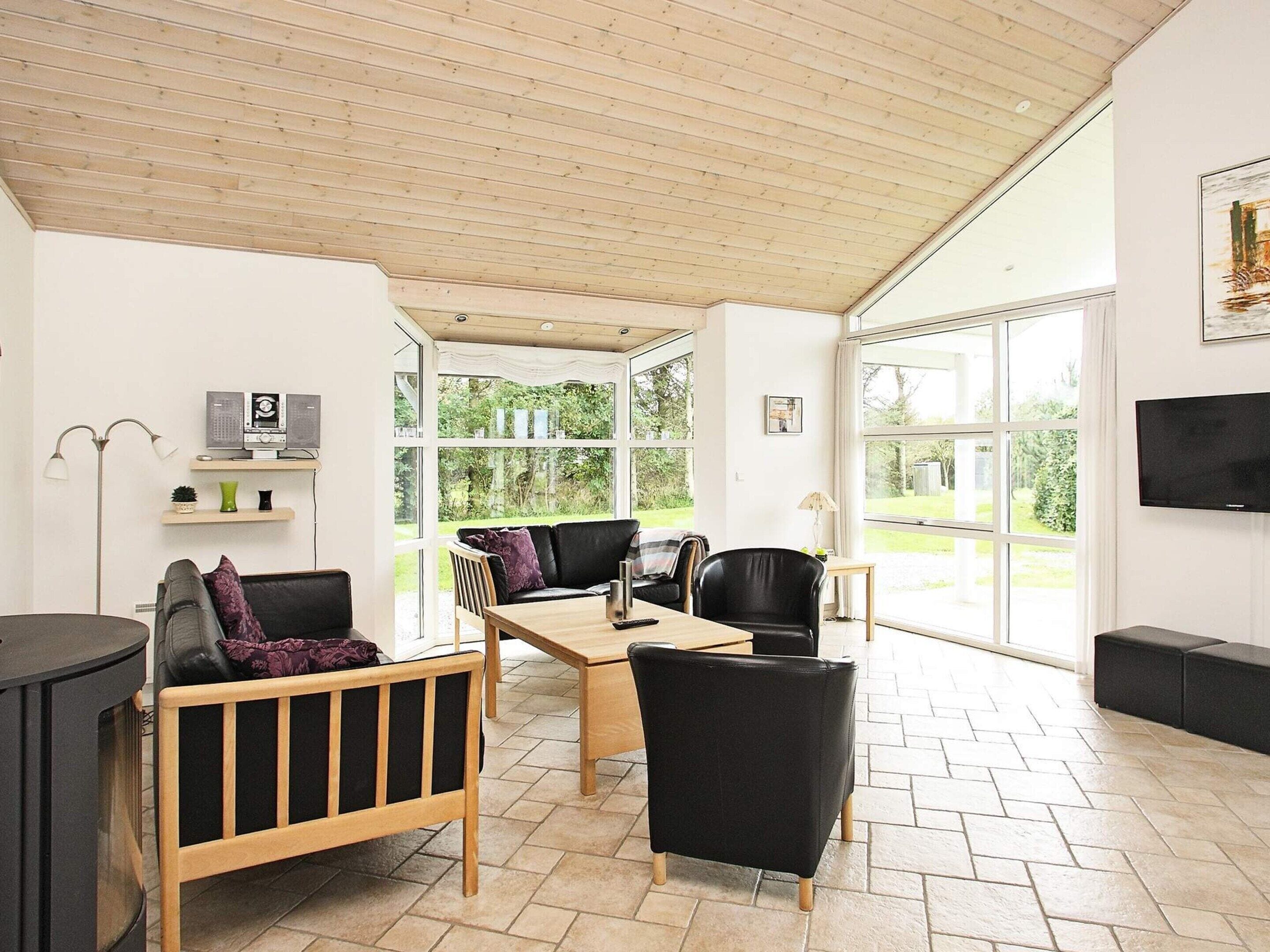 Ein modernes Wohnzimmer mit Holzbalkendecke, großen Fenstern, Kamin und Flachbildfernseher.