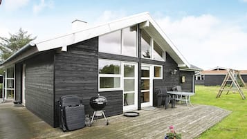 A modern house with a deck, a barbecue grill, and a dining area.