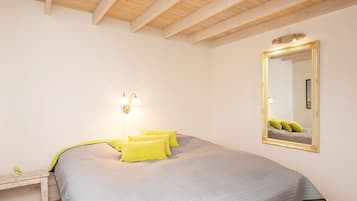 Une chambre à coucher comprenant un lit, une table de chevet, un miroir fixé au mur et un plafond avec des poutres en bois.