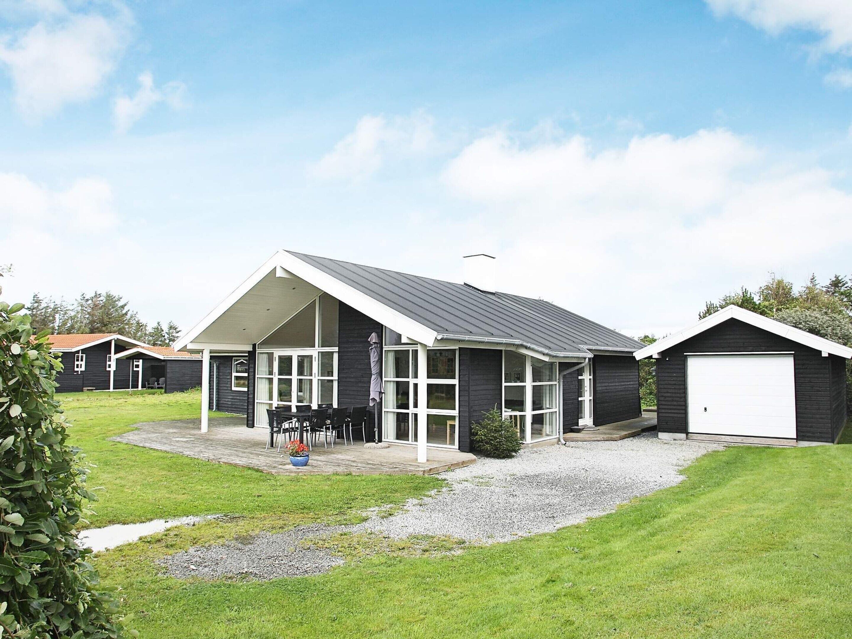 Et moderne hus med en overdækket terrasse, garage og en velplejet græsplæne.