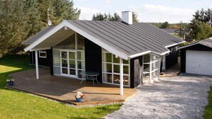 Ein modernes Haus mit geneigtem Dach, großen Fenstern und einer überdachten Terrasse.