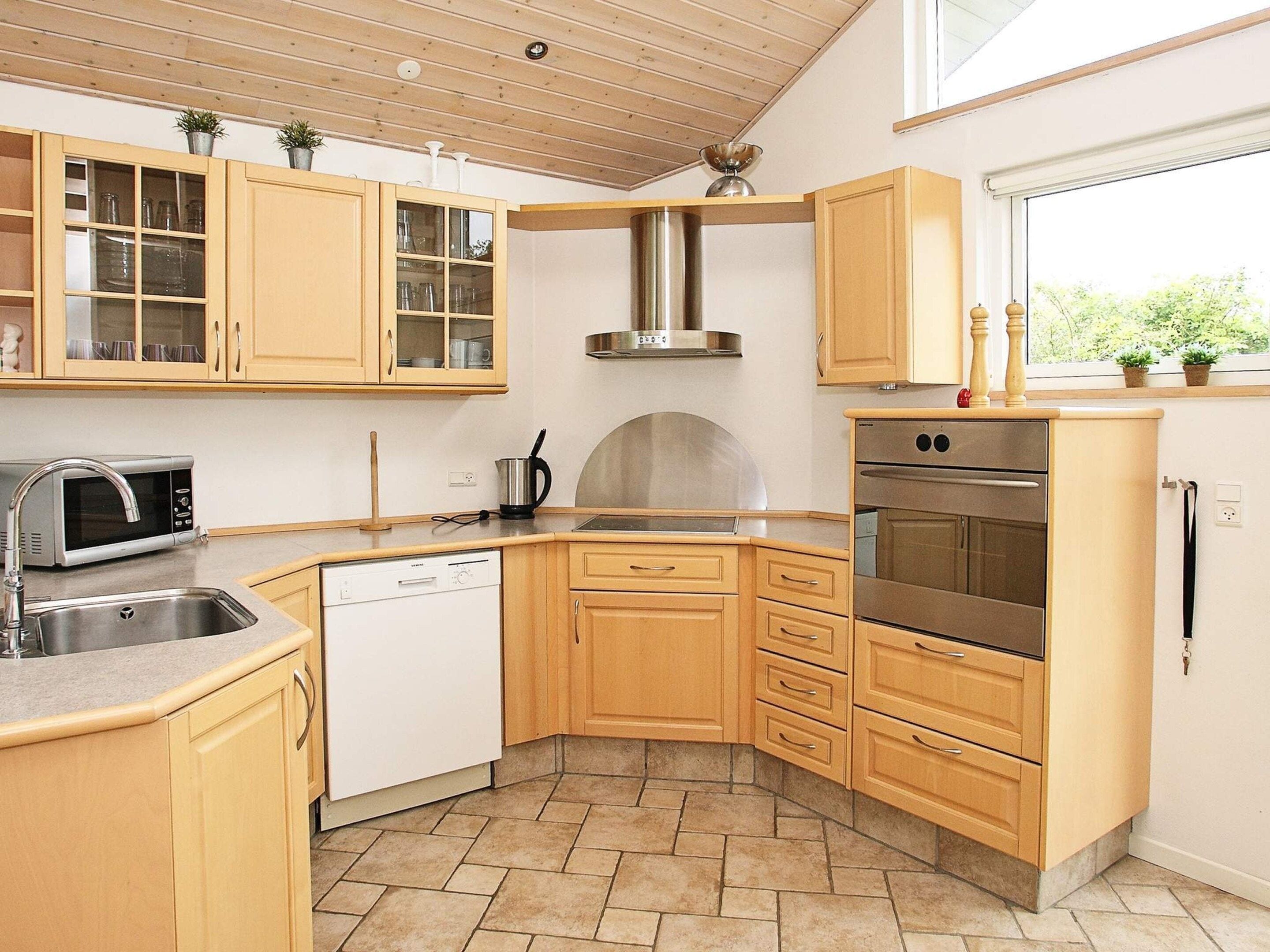A compact kitchen with wooden cabinets, a stainless steel range hood, a built-in dishwasher, and a window providing natural light.