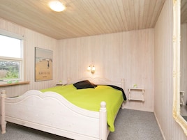 Una habitación con cama, ventana, un cuadro enmarcado, mesita de noche y espejo.