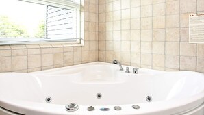 A bathroom with a white bathtub, a window with blinds, and a tiled wall. - 5 Star Holiday Home in Hjorring (Hjørring)