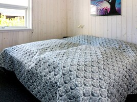 Una habitación con una cama cubierta por un edredón estampado, una ventana con vista a follaje, y un cuadro colgado en la pared.