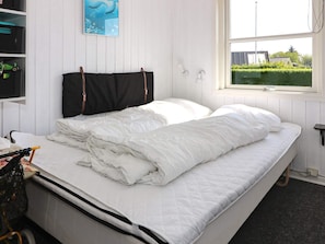 A bed with white bedding, a black headboard, and a window with a view of greenery outside. - Alluring Holiday Home in Hadsund near Sea (Hadsund)