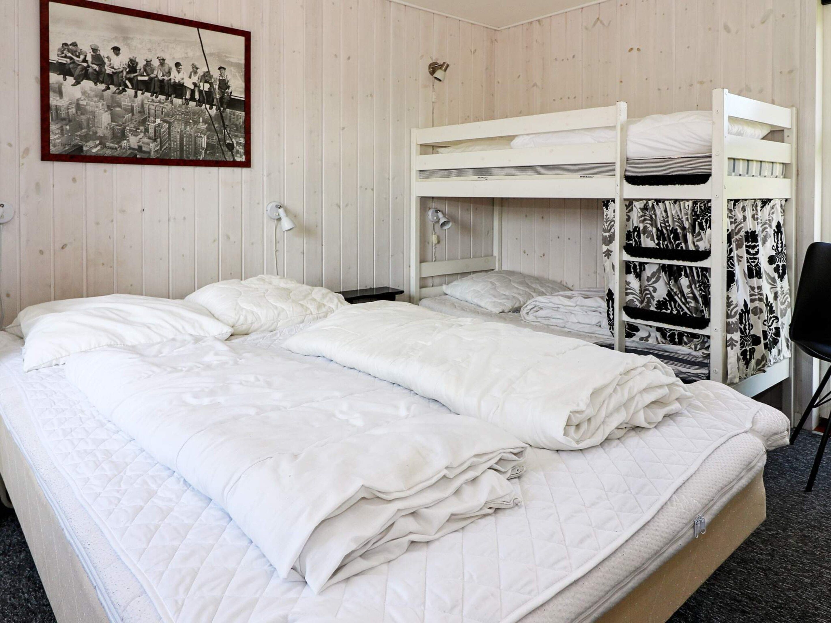 Ein Zimmer mit einem Etagenbett, einem Einzelbett, einem Sessel und einem gerahmten Bild an der Wand.