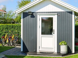 Un cobertizo pequeño con una puerta blanca y una ventana, una bicicleta estacionada afuera, y una planta en maceta junto a la puerta.