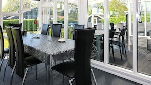 A sunlit room with a table and chairs, large windows, and a view of the outdoors.