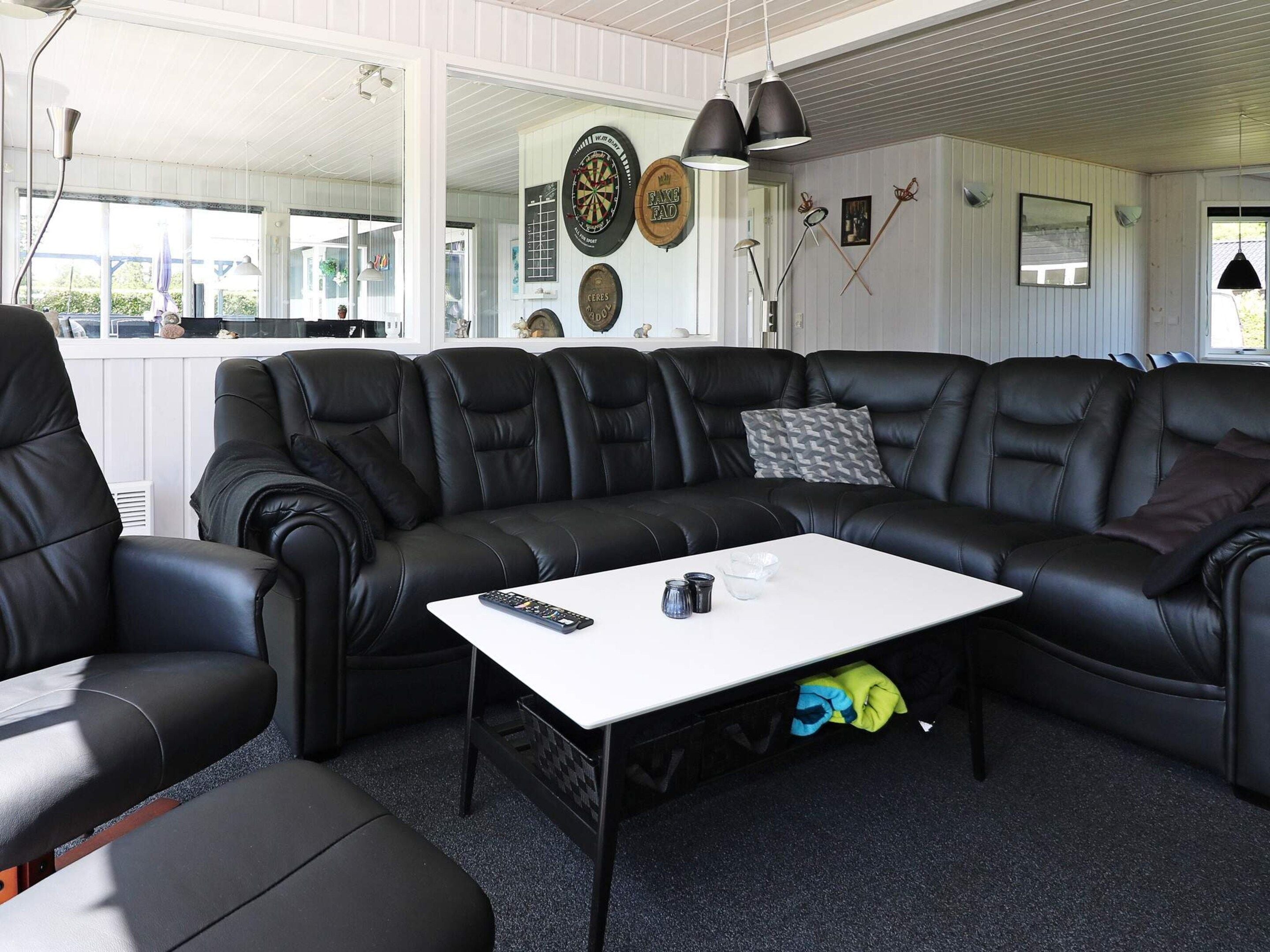 En moderne stue med en sort lædersofa i modulopstilling, et hvidt sofabord og et spiseområde med et hvidt bord og stole.