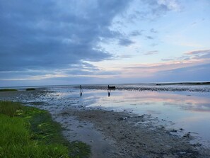 A beach with two people walking, calm water, and a cloudy sky. - Alluring Holiday Home in Hadsund near Sea (Hadsund)