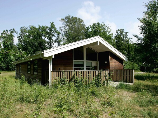 A small cabin with a wooden exterior, a porch, and a fenced yard.