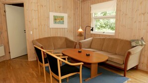 Ein Zimmer mit einer Holzwand, einem beigen Sofa, einem Holztisch und zwei Stühlen.