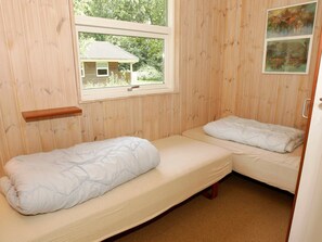A small, single-room cabin with two beds, a window, and wooden walls.