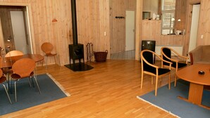 Ein Zimmer mit Holzwänden, einem schwarzen Holzofen, einem Esstisch mit Stühlen, einem Fernseher und einem Korb.