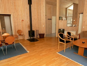 A room with wooden walls, a black wood stove, a dining table with chairs, a television, and a basket.