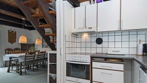 A kitchen with white cabinets, a stove, and a dining area with a table and chairs. - Cozy Holiday Home in Hemmet near Sea (Hemmet)