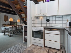 A kitchen with white cabinets, a stove, and a dining area with a table and chairs. - Cozy Holiday Home in Hemmet near Sea (Hemmet)