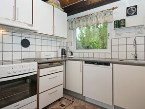 A kitchen with white cabinets, a stove, a dishwasher, and a window with a view of greenery. - Cozy Holiday Home in Hemmet near Sea (Hemmet)
