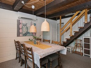 A dining area with a wooden table, chairs, pendant lights, and a staircase.