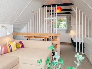 A cozy room with a bunk bed, a sofa with colorful pillows, a hanging light fixture, and a view of greenery outside.