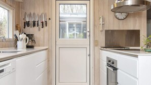 A kitchen with white cabinets, a stainless steel range hood, a clock, and various knives on the wall. - 5 Star Holiday Home in Glesborg (Glesborg)