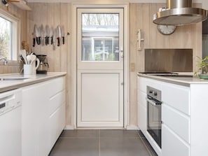A kitchen with white cabinets, a stainless steel range hood, a clock, and various knives on the wall. - 5 Star Holiday Home in Glesborg (Glesborg)