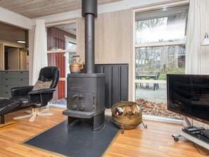 A living room with a black wood-burning stove, a leather chair, a television, and a window with a view of the outdoors. - 5 Star Holiday Home in Glesborg (Glesborg)