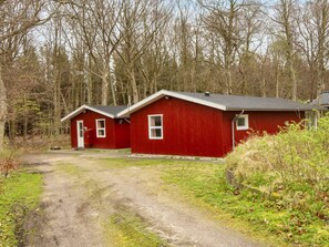 Une cabane rouge, accessible par un chemin de terre, entourée d’arbres.