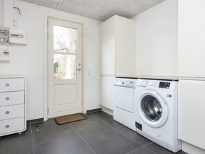 Une buanderie équipée d’un lave-linge à chargement frontal, d’un meuble blanc et d’une porte avec une fenêtre.