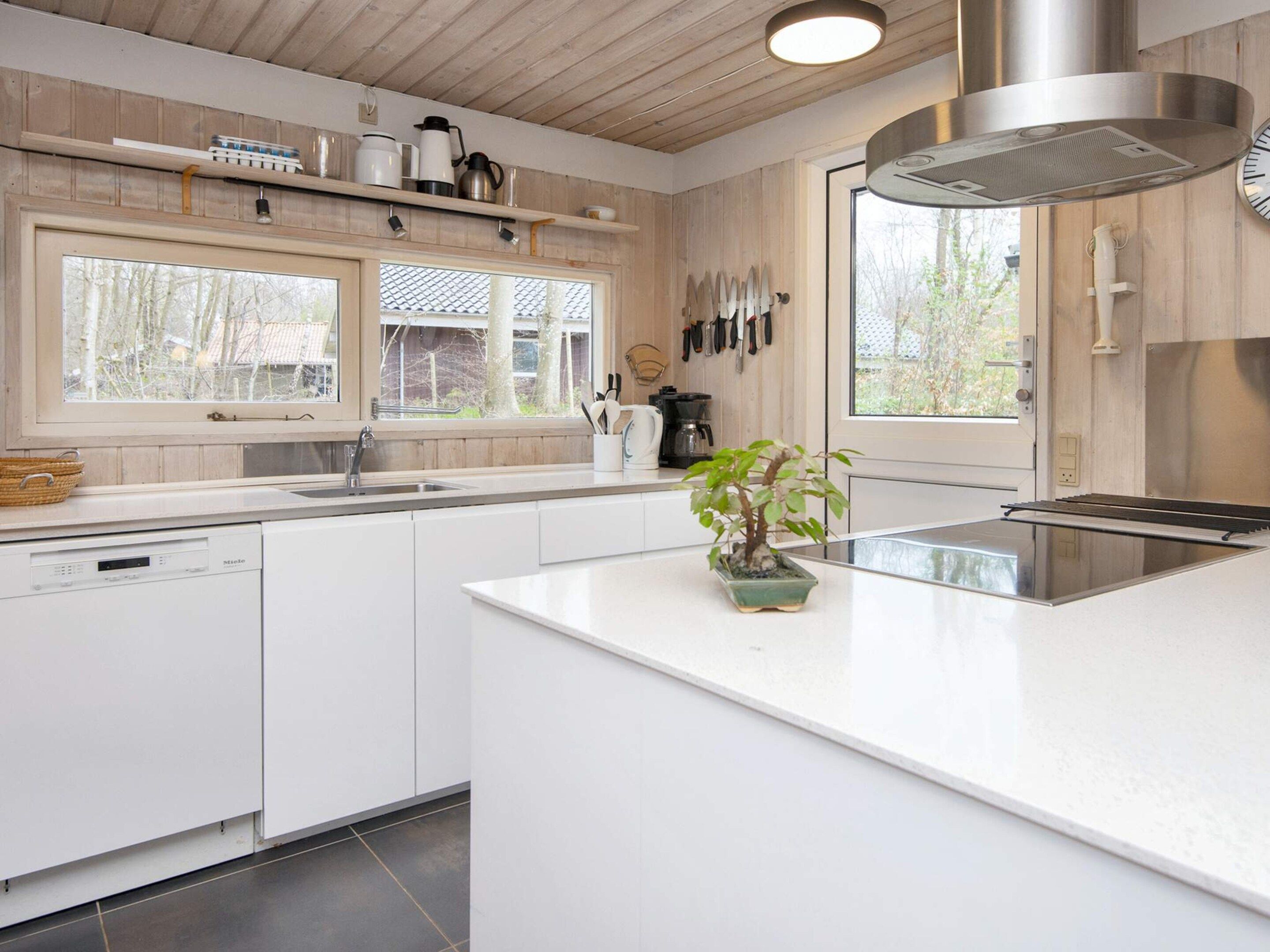 A modern kitchen with white cabinetry, a built-in dishwasher, a large island with a plant, and a window providing natural light.