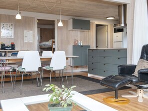 A modern living room with a dining area, a black leather sofa, and a wooden ceiling.