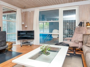 Un salon moderne doté d’un téléviseur à écran plat, d’un canapé confortable, d’une table basse en verre agrémentée d’une plante, et offrant une vue sur une piscine grâce à de grandes fenêtres.