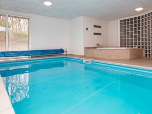 Une piscine à l’eau d’un bleu cristallin, une serviette bleue posée sur le bord, et un espace jacuzzi intégré.
