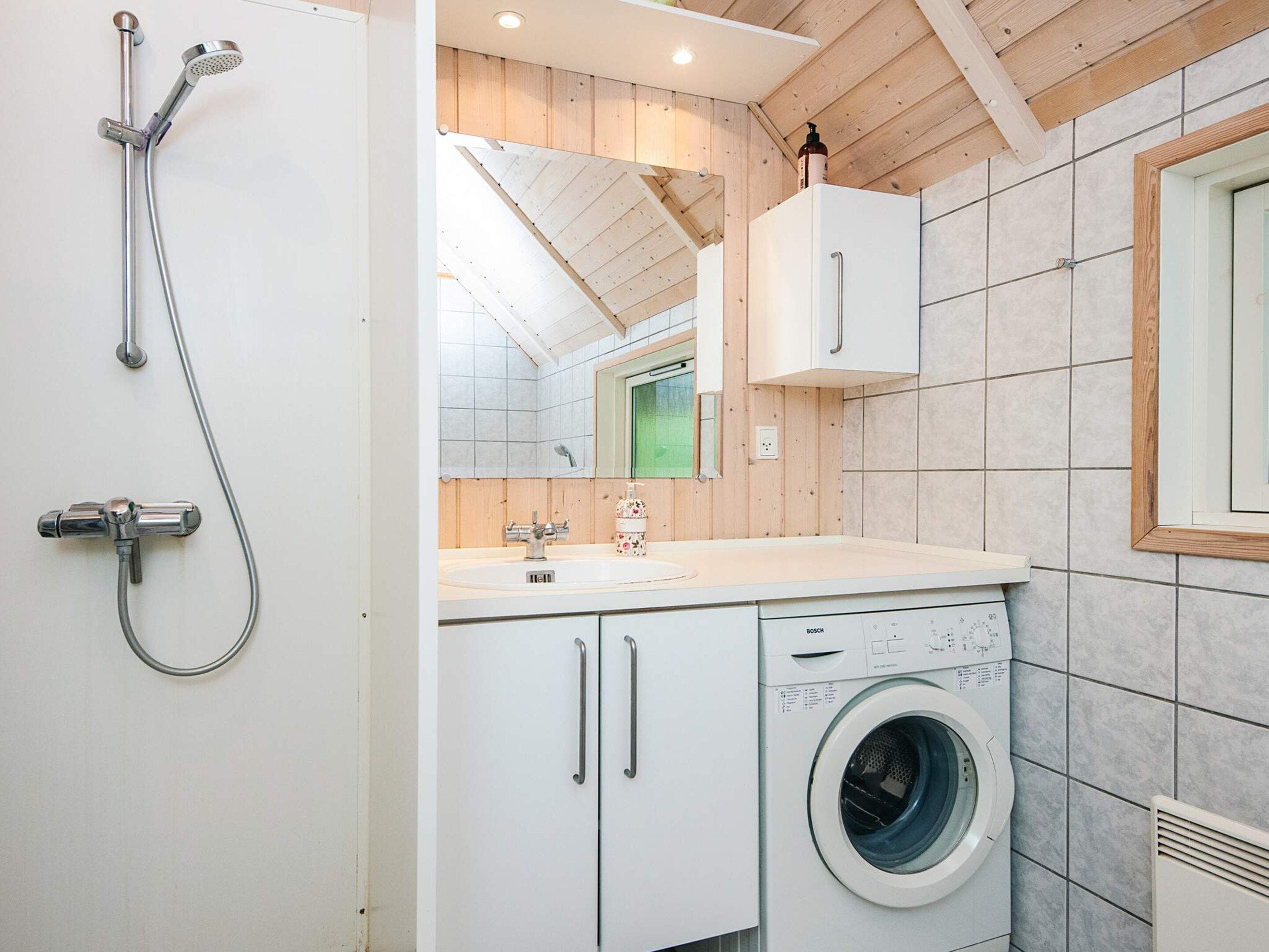 A modern bathroom with a shower, a washing machine, and a mirror.
