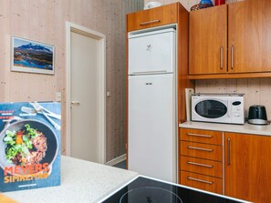 A compact kitchen with wooden cabinets, a white refrigerator, a microwave, and a coffee maker. - 4 Star Holiday Home in Blavand (Blavand)