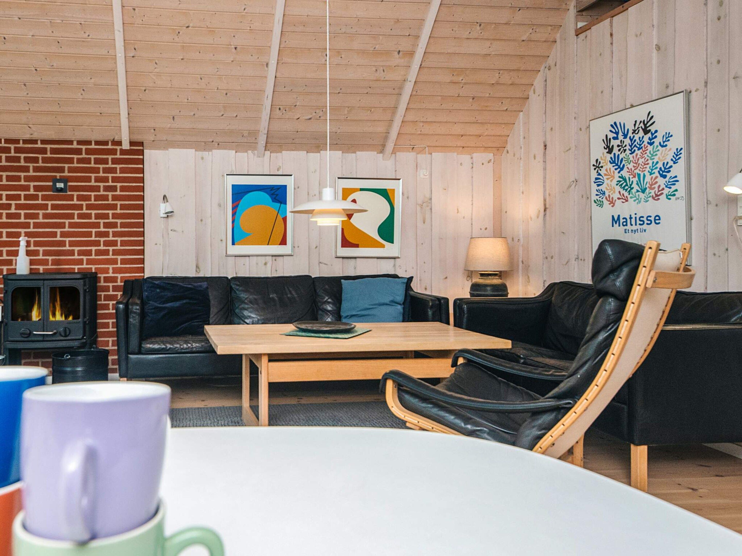 Une pièce chaleureuse avec une cheminée, un canapé, une table à manger et des œuvres d’art accrochées aux murs.