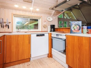 A kitchen with wooden cabinets, a dishwasher, an oven, and a window with a view of greenery. - 4 Star Holiday Home in Blavand (Blavand)