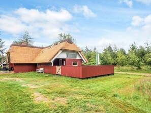 A red barn with a thatched roof and a white door, surrounded by a grassy field and trees. - 4 Star Holiday Home in Blavand (Blavand)