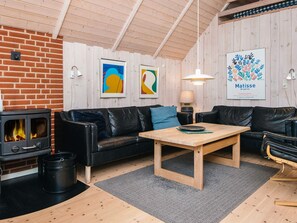 A cozy living room with a fireplace, a black leather sofa, a wooden coffee table, and a framed artwork of Matisse. - 4 Star Holiday Home in Blavand (Blavand)
