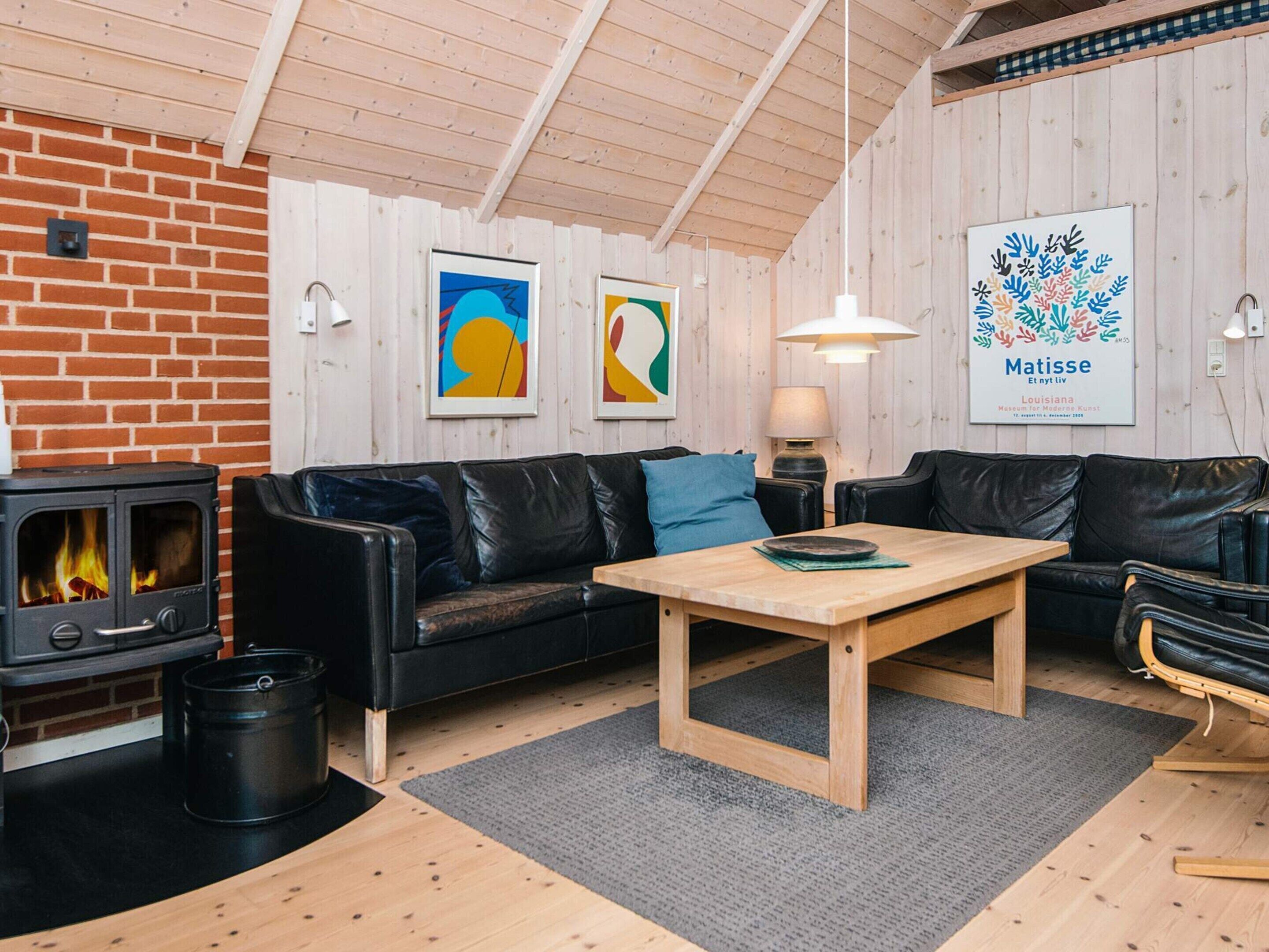 A cozy living room with a black leather sofa, a wooden coffee table, a fireplace, and a framed artwork of Matisse.