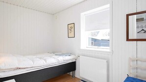 Um quarto com uma cama, um radiador, uma janela, uma cadeira e um tapete listrado.